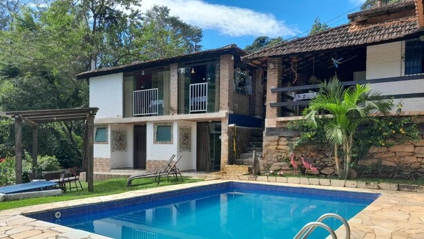 A swimming pool with stone tiles, a two-story building with a balcony, and a pergola. - Pousada Estância Vip (Cunha)
