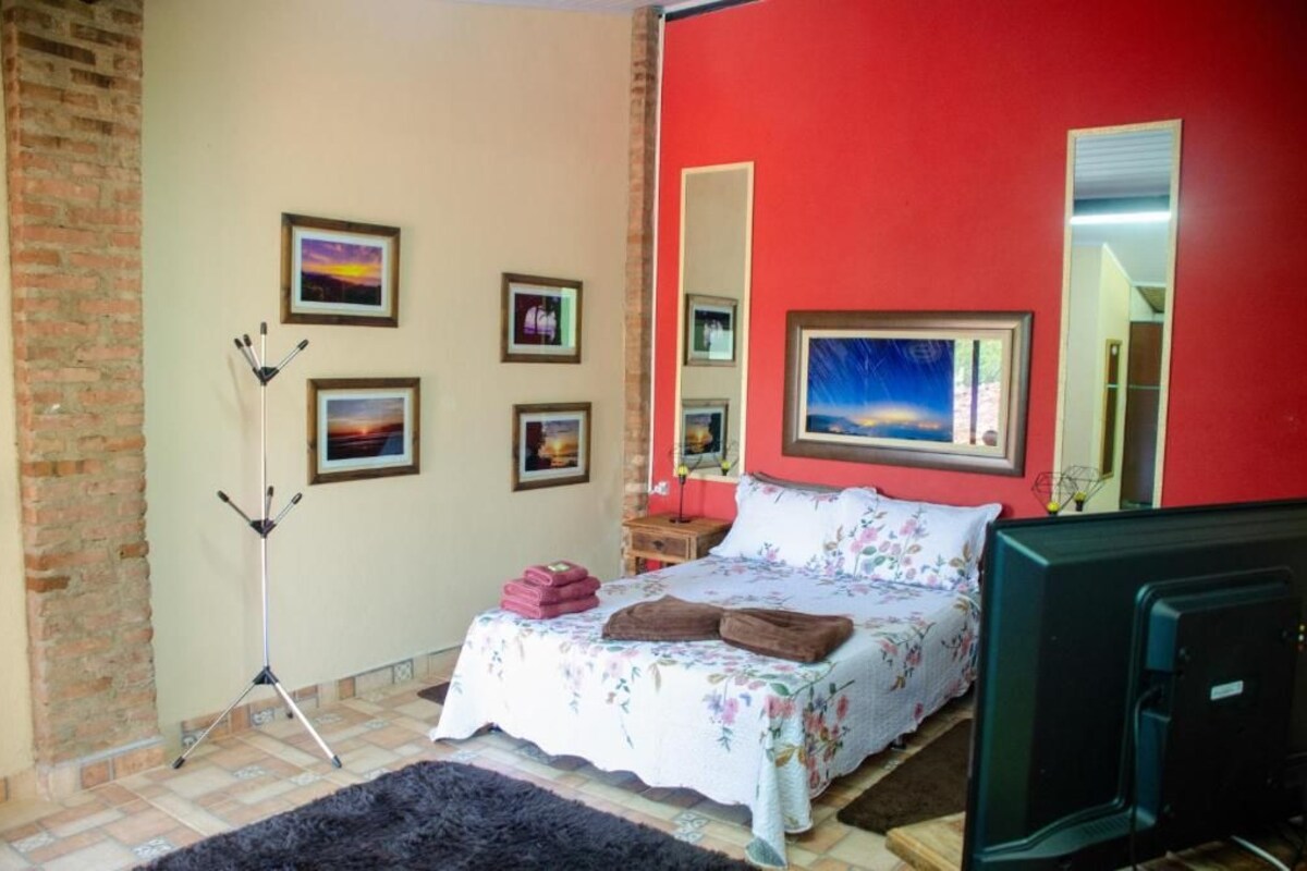 Un dormitori amb un llit, una televisió, una làmpada de trípode i diverses fotografies emmarcades a la paret.