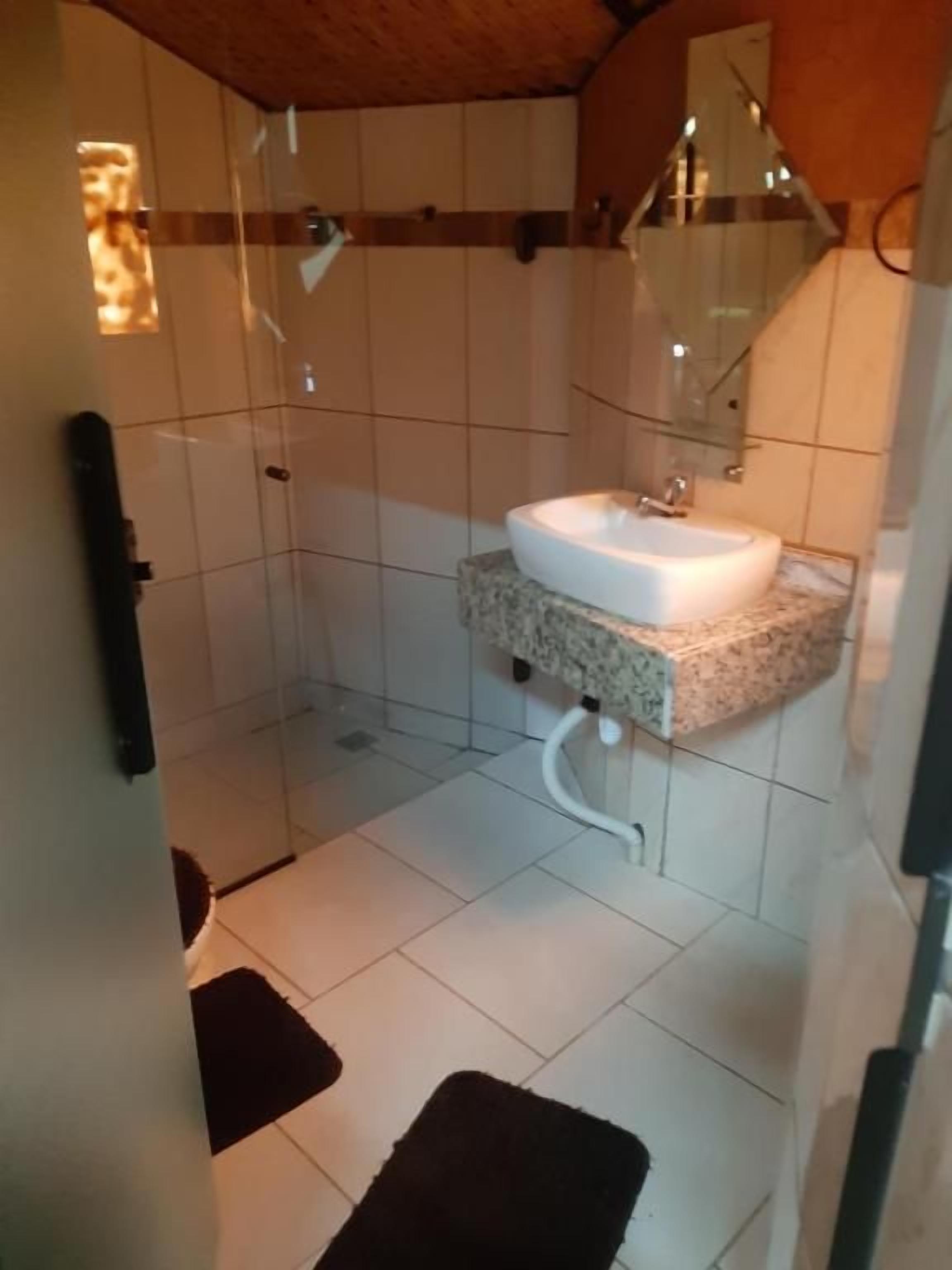 Un baño con lavamanos blanco, cabina de ducha de vidrio y suelo con baldosas.