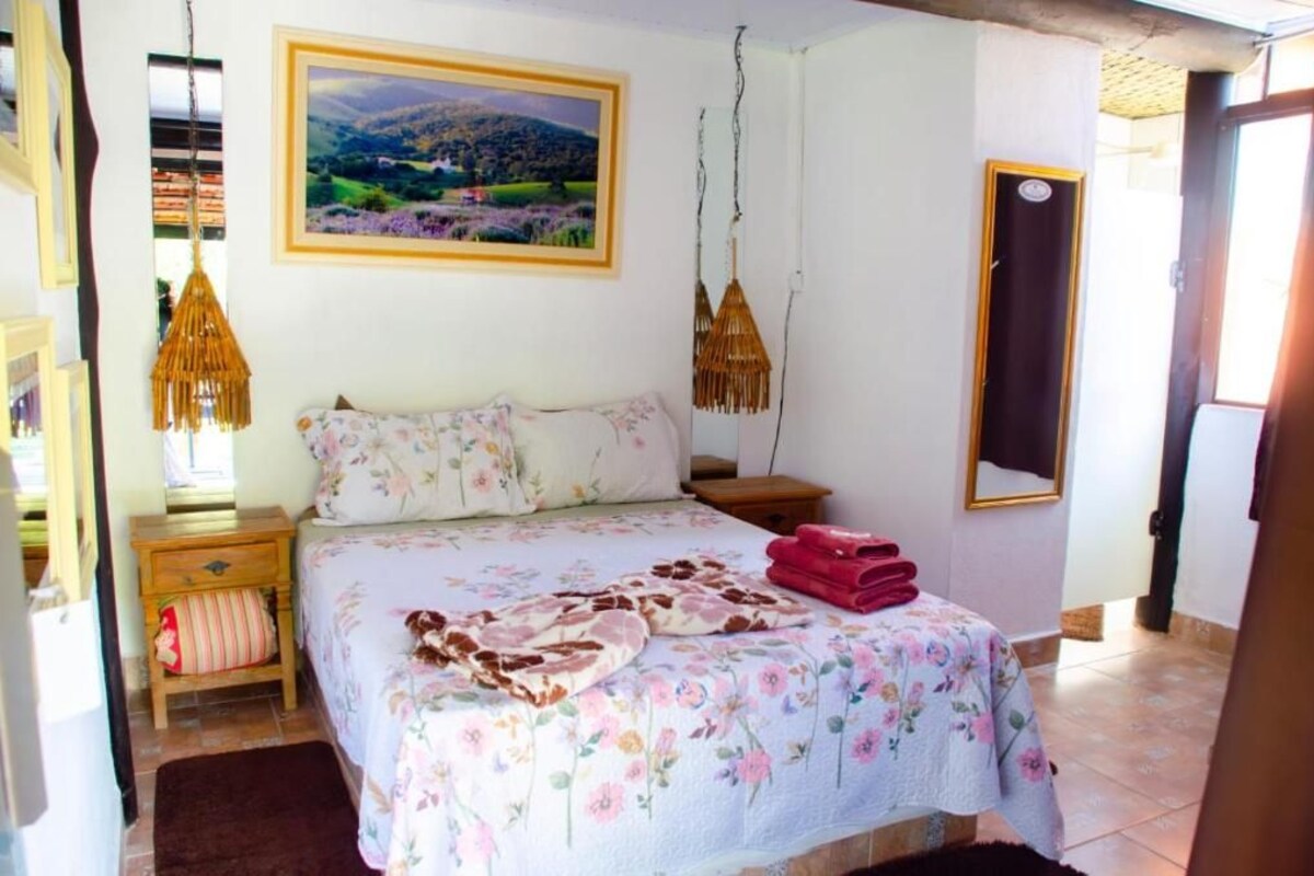 Un dormitori amb llit, una taula de nit, una làmpada penjant, un quadre a la paret i una porta.