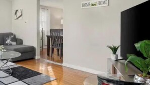 A modern living room with a sofa, a glass coffee table, and a dining area in the background. - 2-bedroom bed & breakfast in nice Syracuse with front fenced in yard (Syracuse)