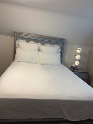 A neatly made bed with a headboard, a bedside table with a lamp, and a wall-mounted light fixture. - 2-bedroom bed & breakfast in nice Syracuse with front fenced in yard (Syracuse)