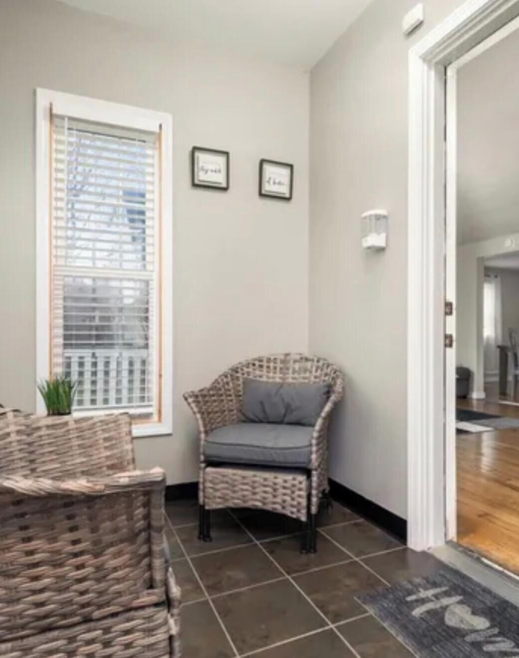 A corner room with a wicker chair, a small table, and a window with blinds.