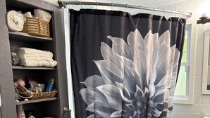 Un baño con inodoro, cortina de ducha con diseño floral, repisa con artículos de aseo y toallero.