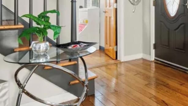 Una escalera que lleva a un cuarto con una puerta de madera oscura, una mesa de vidrio con una planta y una silla de metal.