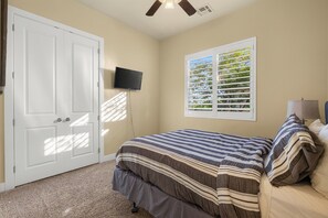 Ein Schlafzimmer mit einem Bett, einem Fernseher, einem Fenster mit Jalousien und einem Deckenventilator.