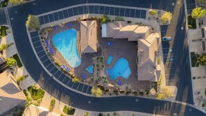 Luchtfoto van een resort met meerdere zwembaden, een parkeerplaats en een gebouw met een schuin dak.
