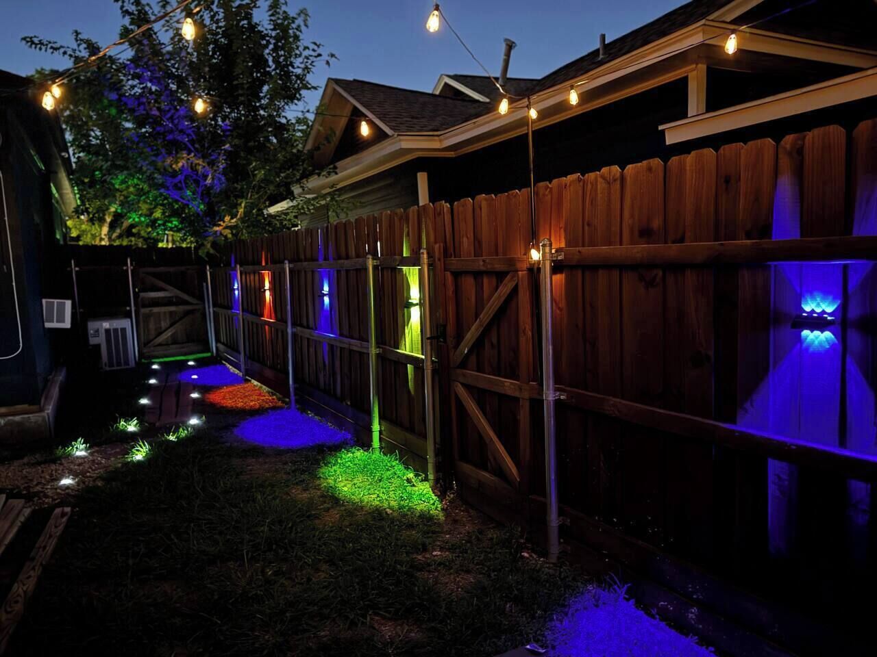 A backyard with a wooden fence, string lights, and a small garden area.