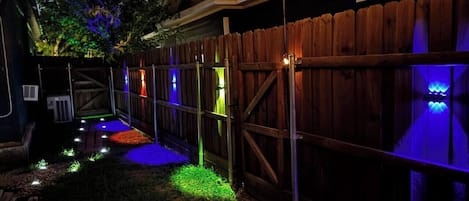 A backyard with a wooden fence, string lights, and a small garden area.