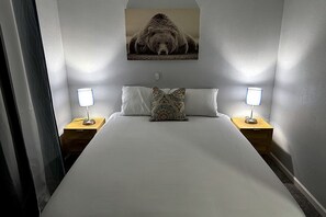 A hotel room with a large bed, two bedside tables with lamps, a patterned pillow, and a wall-mounted picture. - Cozy Bungalow-Dallas Central (Dallas)