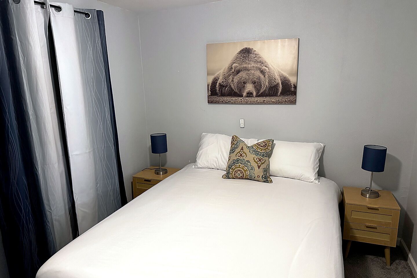 A hotel room with a bed, two bedside tables with lamps, a wall-mounted picture, and a curtain.