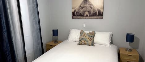 A hotel room with a bed, two bedside tables with lamps, a wall-mounted picture, and a curtain.