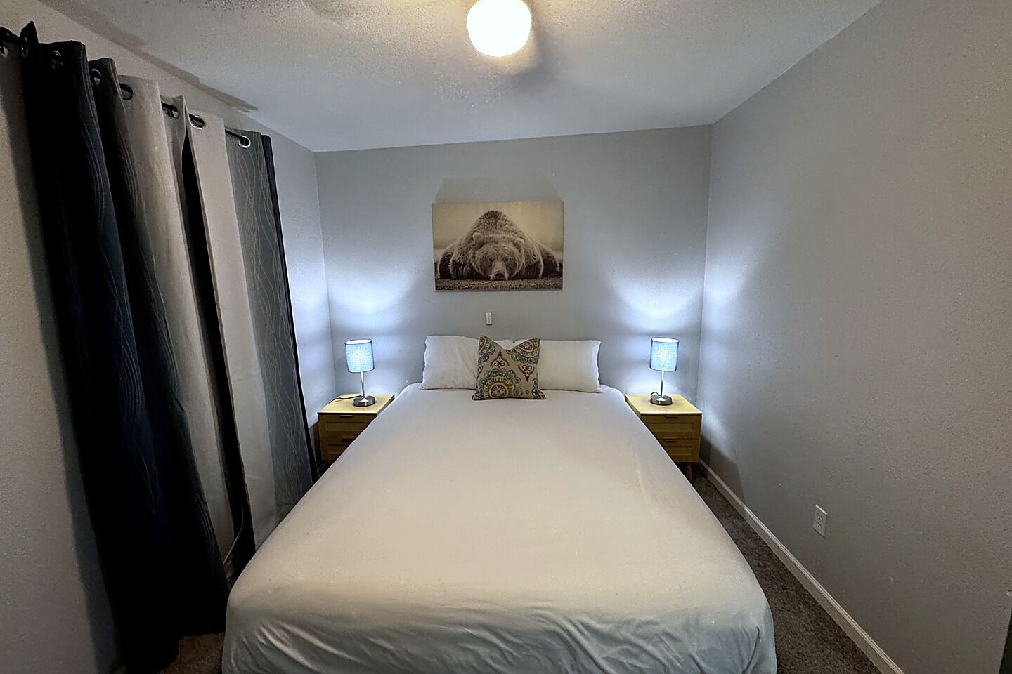 A bedroom with a bed, two bedside lamps, a wall-mounted picture, and a ceiling light.