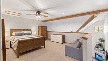 A bedroom with a bed, a nightstand, a dresser, a ceiling fan, and a small seating area with a sofa and a TV.