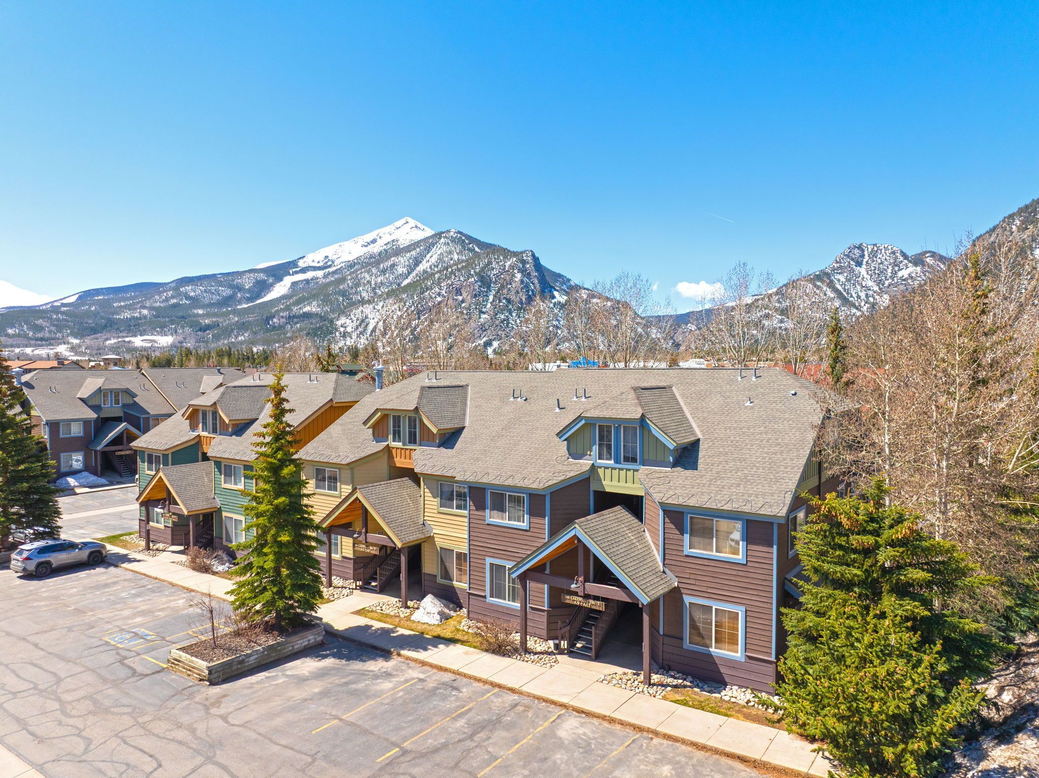 A row of multi-story buildings with a parking lot in front, set against a backdrop of snow-capped mountains.