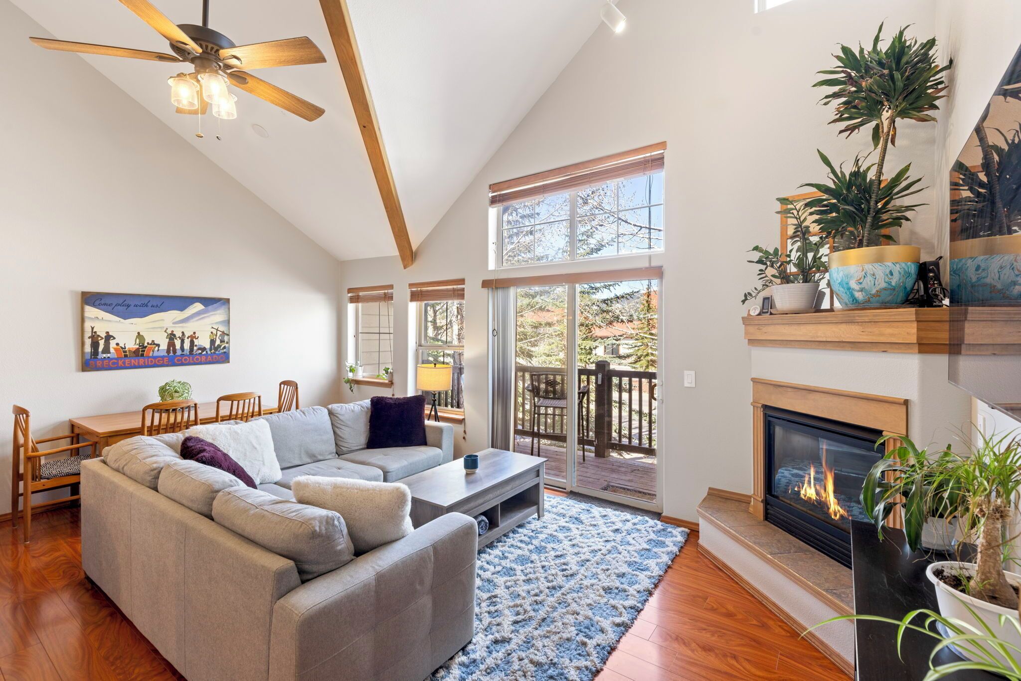 A spacious living room with a fireplace, a ceiling fan, and a large window.