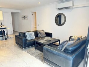 Un salon moderne avec un canapé en cuir noir, une table basse et un grand miroir rond accroché au mur.