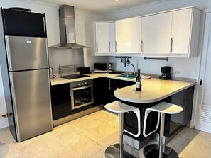Cozinha moderna com eletrodomésticos de aço inoxidável, uma ilha central com banquetas e armários brancos.