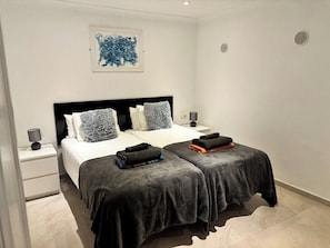 A modern bedroom with a large bed, two bedside tables, a headboard, and a wall-mounted artwork. - 2 Bedroom Beachfront Playa Flamingo Apartment with Private Terrace & Air Con (Playa Blanca)