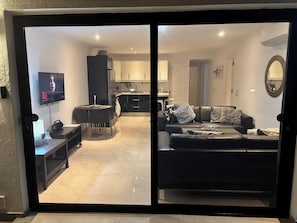 A modern living room with a black sofa, a TV mounted on the wall, and a dining area with a table and chairs. - 2 Bedroom Beachfront Playa Flamingo Apartment with Private Terrace & Air Con (Playa Blanca)