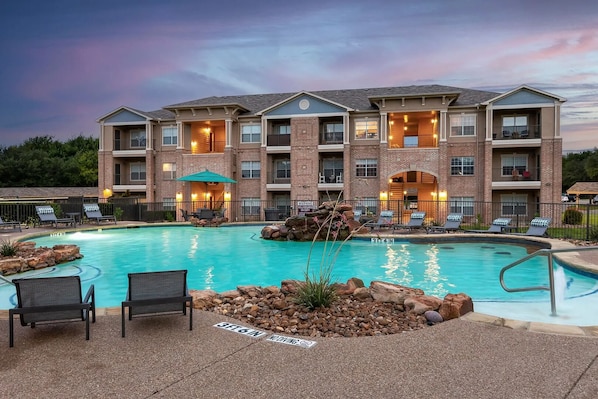 A multi-story hotel with a swimming pool, outdoor seating, and a landscaped area. - Landing Stunning 1bd, Gym (McKinney)