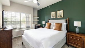 A bedroom with a bed, bedside tables, a desk, a chair, a window with blinds, and a ceiling fan. - Landing Stunning 1bd, Gym (McKinney)