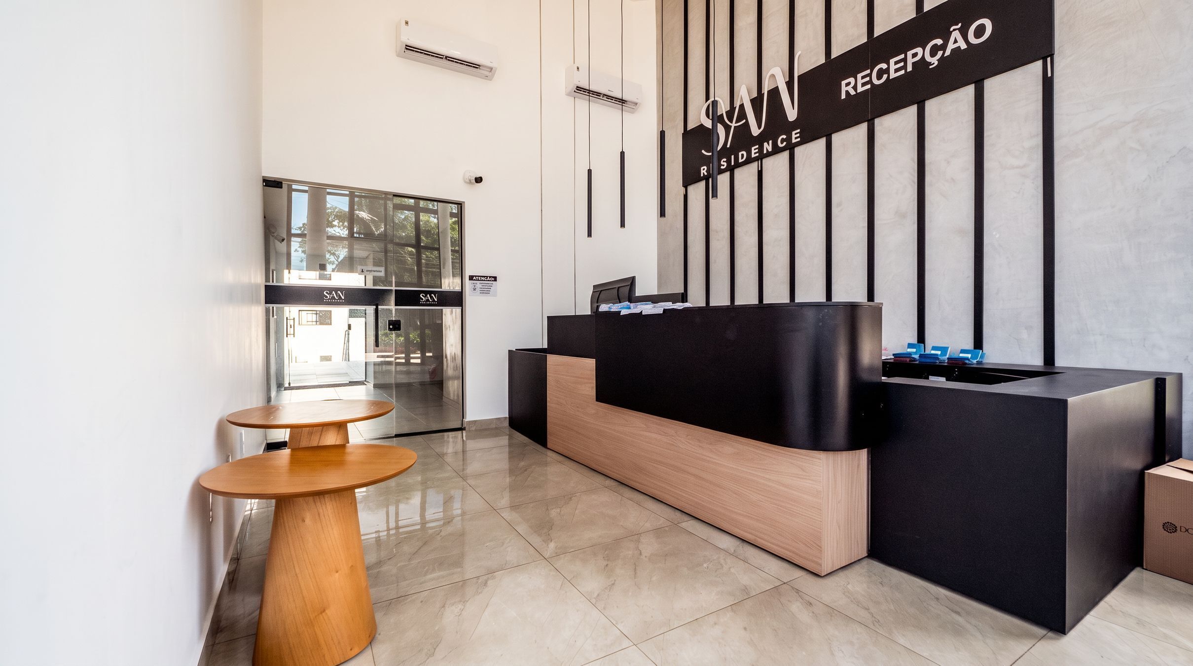 A reception area with a reception desk, a seating area with a table, and a glass door leading to a room.