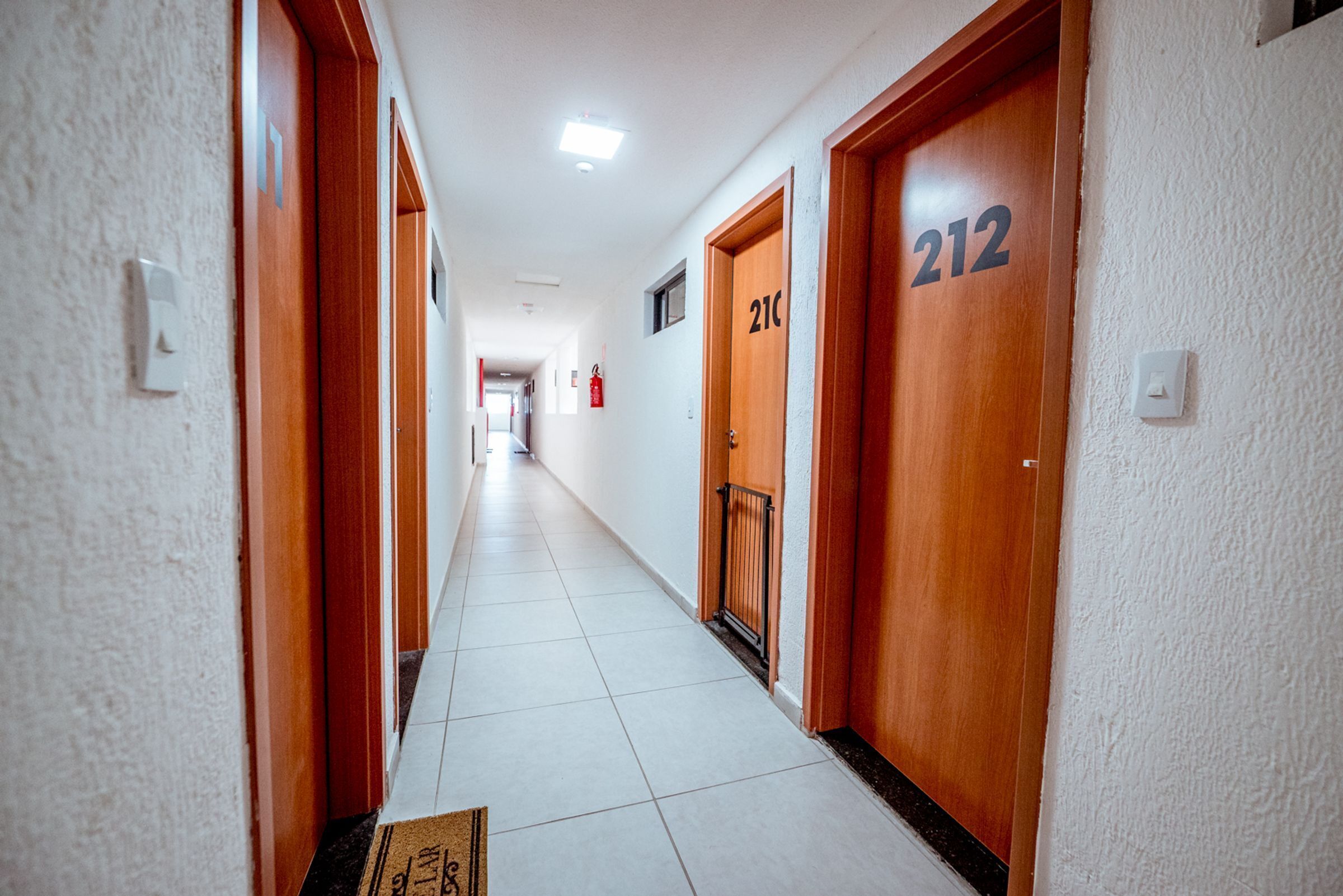 Corredor de hotel com portas de madeira, com os números 212 e 213, e um extintor de incêndio na parede.