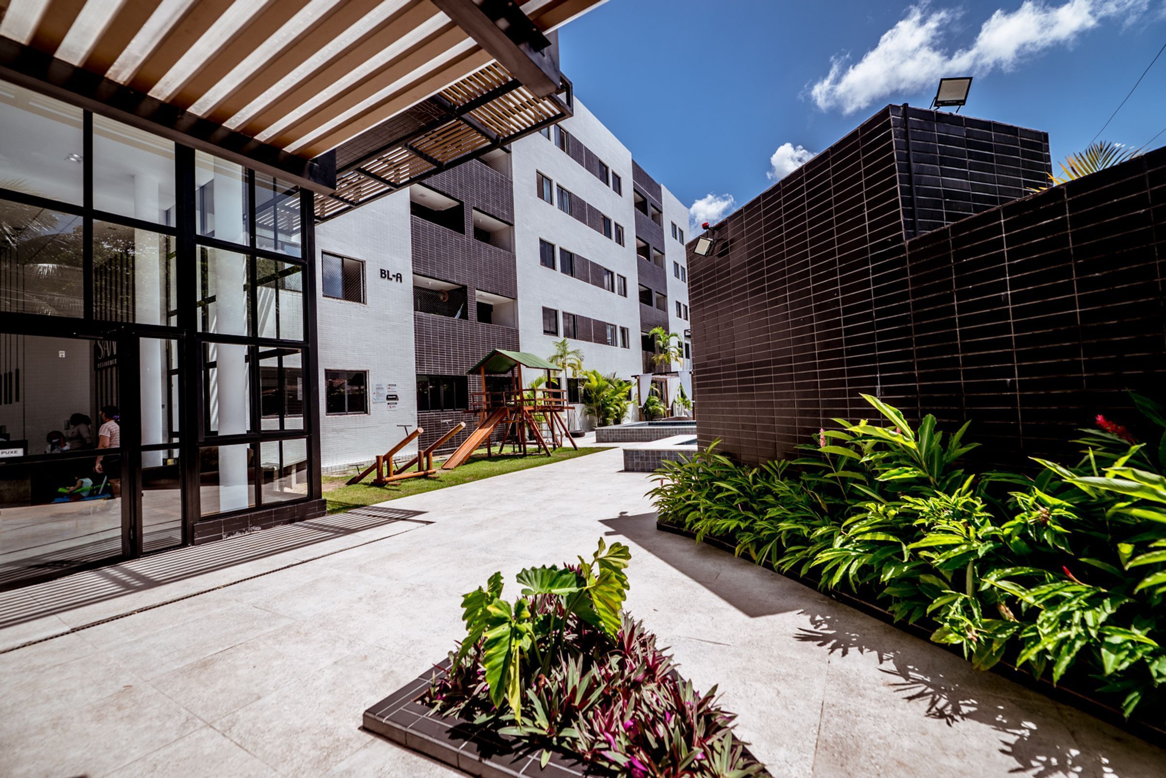 Un bâtiment moderne doté de grandes fenêtres, d’un espace extérieur couvert et d’une aire de jeux.