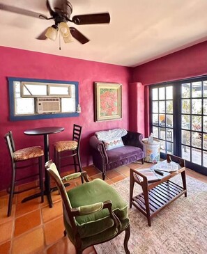 A room with a ceiling fan, a window with blinds, a sofa, a green armchair, a wooden table, and a tiled floor.