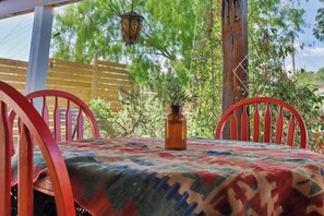 A table with a patterned tablecloth, two red chairs, a brown vase with a plant, and a hanging lantern.