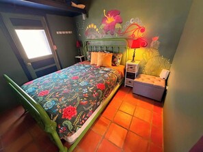 A bedroom with a bed, a nightstand, a lamp, and a wall with floral artwork. - Posada Linda - 4 separate suites 2m to downtown! (Las Cruces)