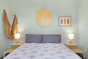 A bedroom with a bed, two bedside tables, a wall hanging, and a framed picture.