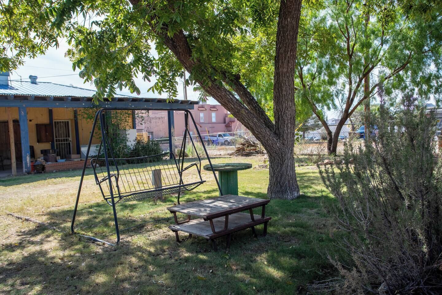 A swing set, picnic table, and a tree in a yard with a building in the background.