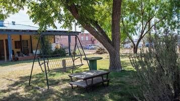 A swing set, picnic table, and a tree in a yard with a building in the background.