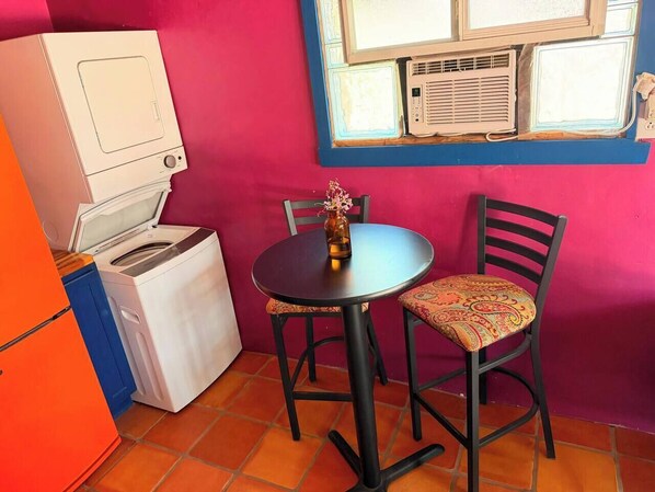 A compact kitchen with a washing machine, a small table, and two chairs.