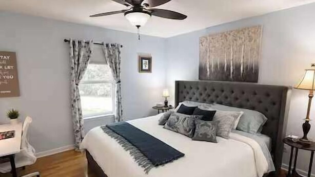 A bedroom with a bed, a desk, a chair, a ceiling fan, and a window with curtains. - Tennessee River Cabin - Loft, Grill & Lake Access (Waverly)