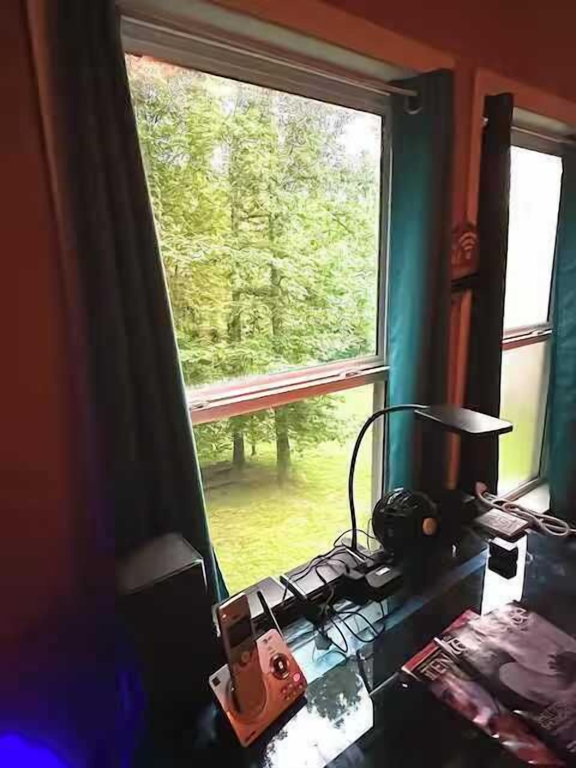 A room with a window overlooking a forest, a desk with a computer, and a chair.