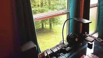 A room with a window overlooking a forest, a desk with a computer, and a chair.