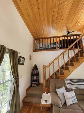 A wooden staircase leading to a loft bedroom, a sofa with cushions, and a bookshelf.