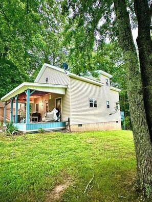 A single-story house with a porch, surrounded by trees.