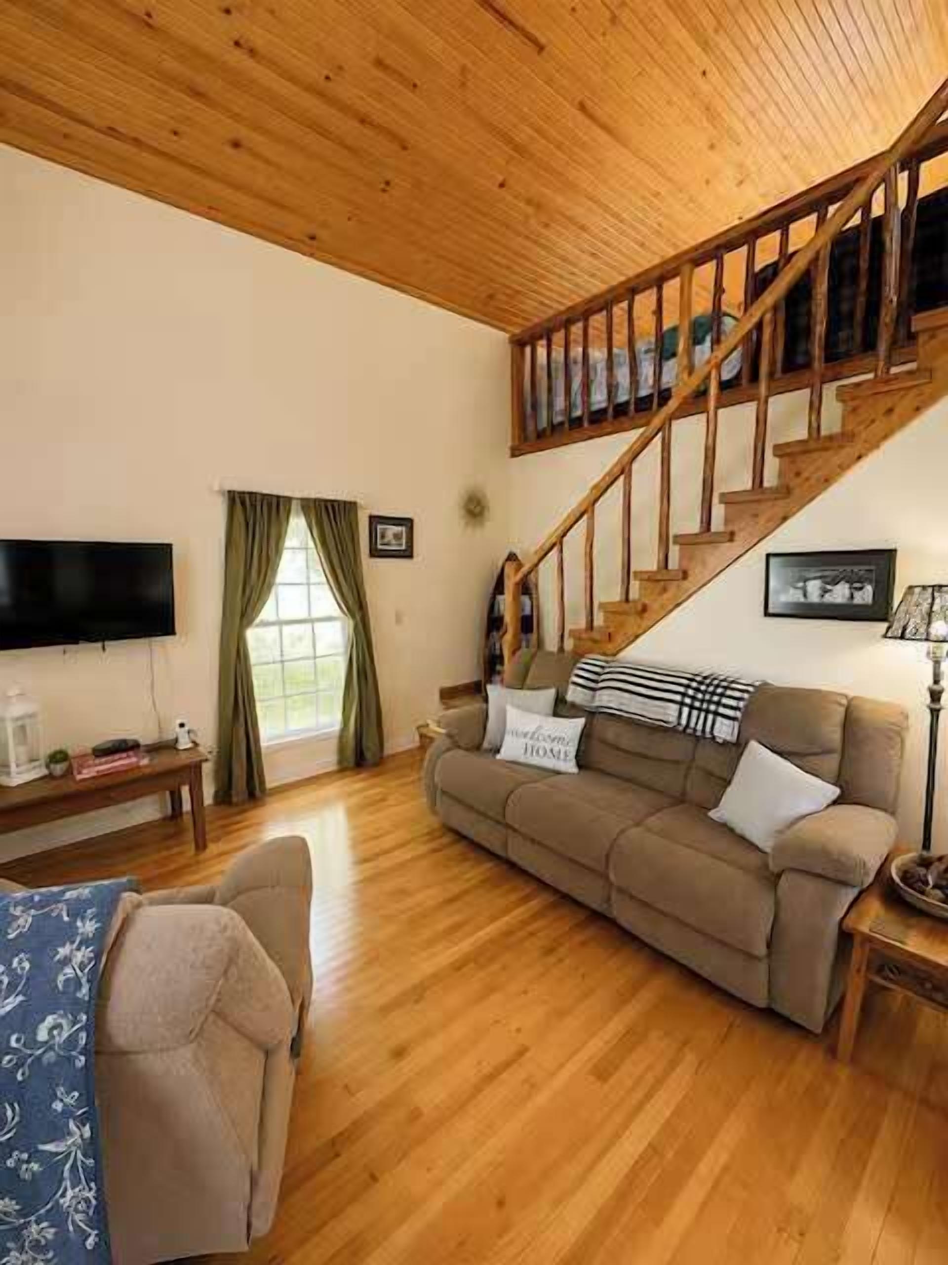 A living room with a wooden staircase, a sofa, a television, and a window with curtains.