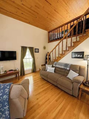 Una sala de estar con una escalera de madera, un sofá, un televisor y una ventana con cortinas.