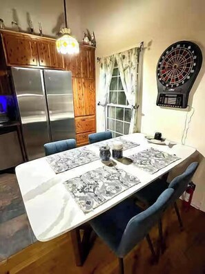 A dining area with a table set for two, a dartboard, and a refrigerator.