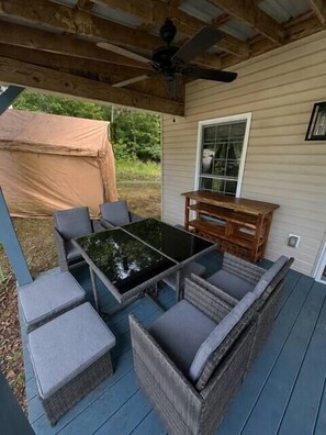 A covered outdoor seating area with a table and chairs, a ceiling fan, and a view of a house.