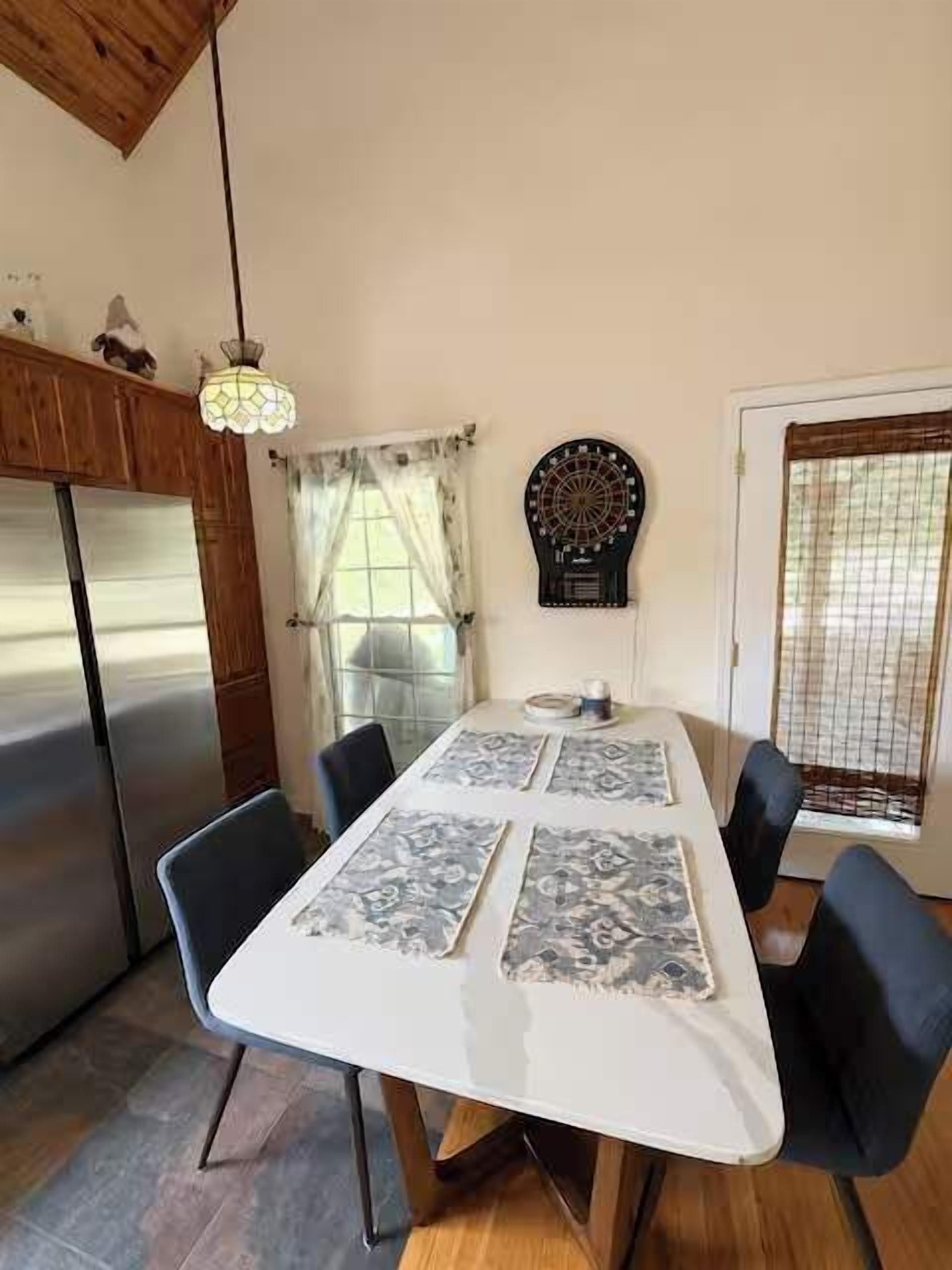 Un área de comedor con una mesa blanca, sillas negras, un dardo y un refrigerador.