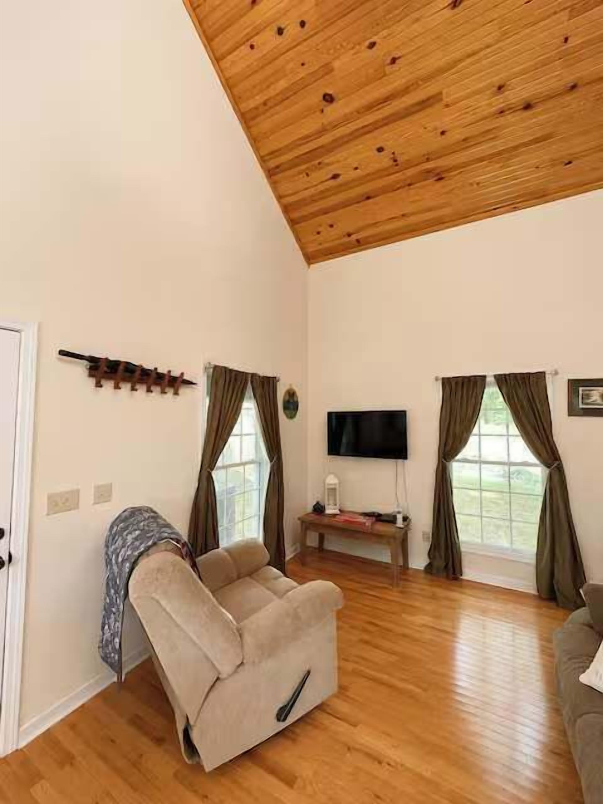 Una sala de estar con techo de madera, un sofá, un televisor y una ventana con cortinas.