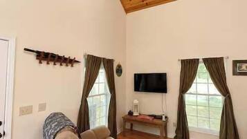 Una sala de estar con techo de madera, un sofá, un televisor y una ventana con cortinas.