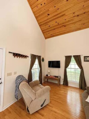 Een woonkamer met een houten plafond, een bank, een televisie en een raam met gordijnen.