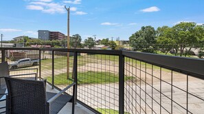 Ein Balkon mit Metallgeländer, der auf einen Parkplatz und Gebäude blickt.